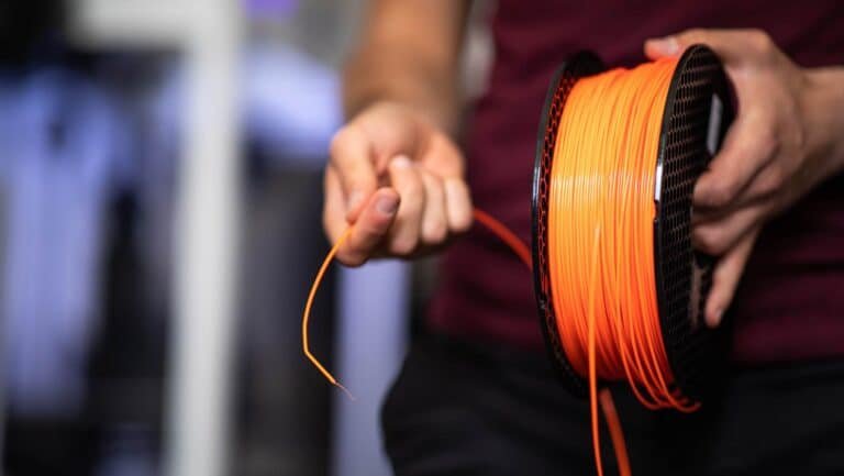 Person holding a roll of orange 3D printer filament